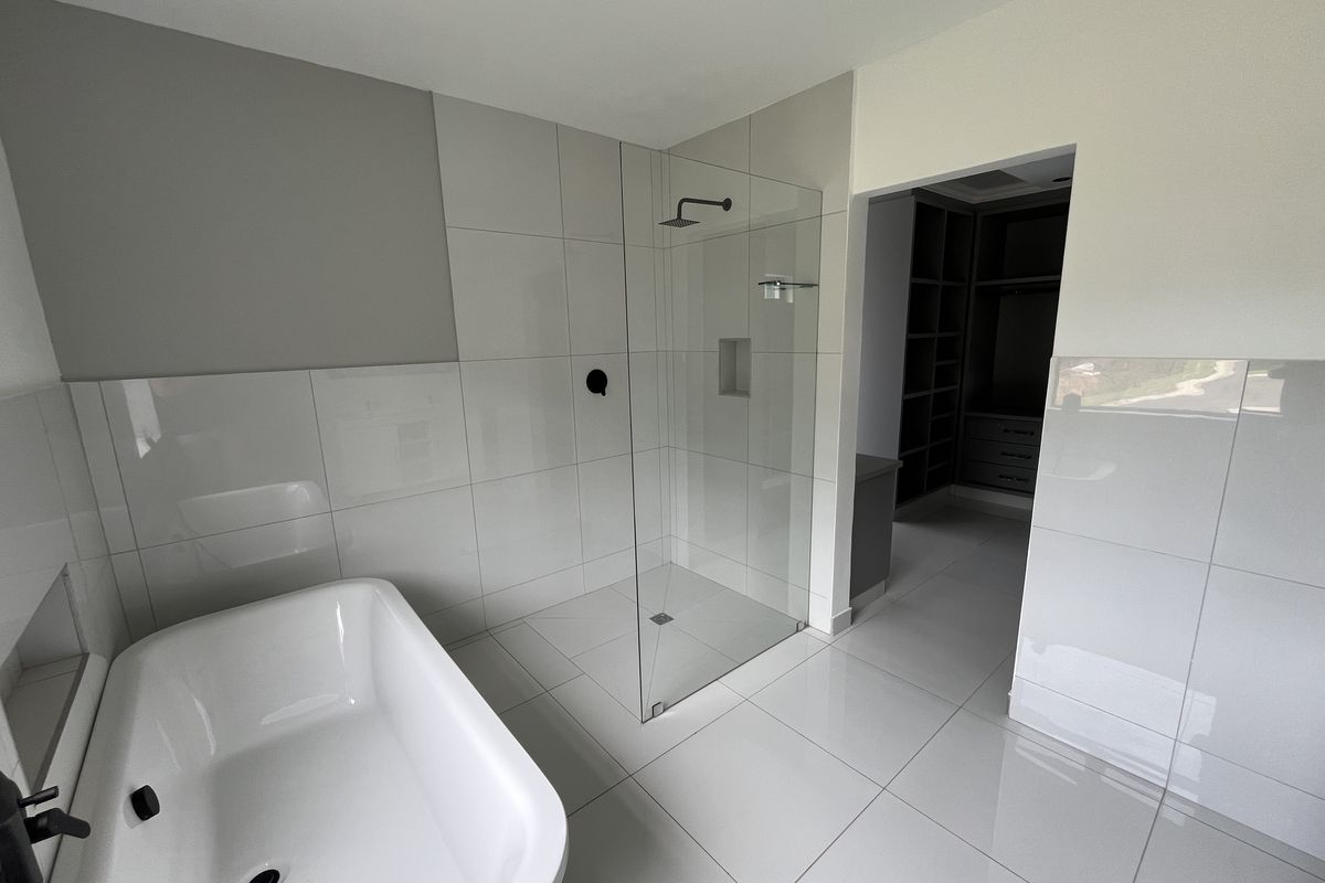 Modern bathroom featuring a freestanding bathtub, a frameless glass walk-in shower with matte black fixtures, and large-format neutral floor and wall tiles.