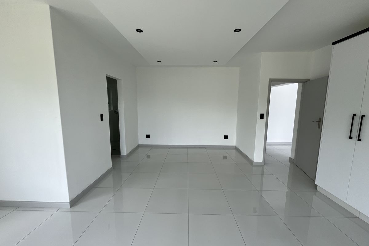 A bright, modern, and empty living area featuring neutral tiled flooring, recessed ceiling lighting, and built-in cabinetry.