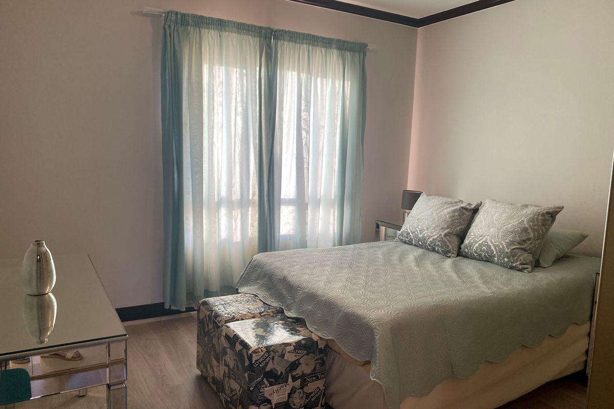 A well-lit bedroom featuring light wood-look flooring, dark crown molding, and a large window with sheer curtains.