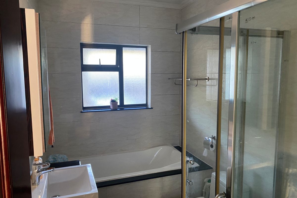 A modern bathroom featuring a tiled bathtub, a separate glass-enclosed shower, a vanity basin, and a window with privacy glass.