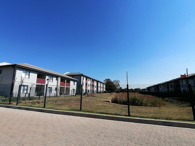 Exterior view of a townhouse complex featuring multi-story residential blocks, paved driveway access, and perimeter security fencing.