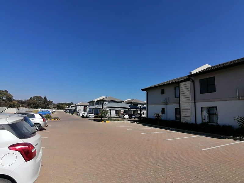 A view of the townhouse complex exterior featuring paved parking areas, carports, and multi-story residential units under a clear blue sky.