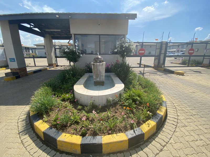 The entrance to the townhouse complex features a secure gatehouse, electric fencing, and a landscaped central water feature.