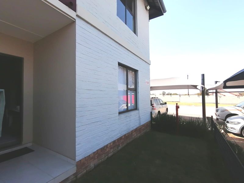 Front exterior view of the townhouse featuring a painted brick facade, tiled entrance area, and adjacent shade cloth carport parking.