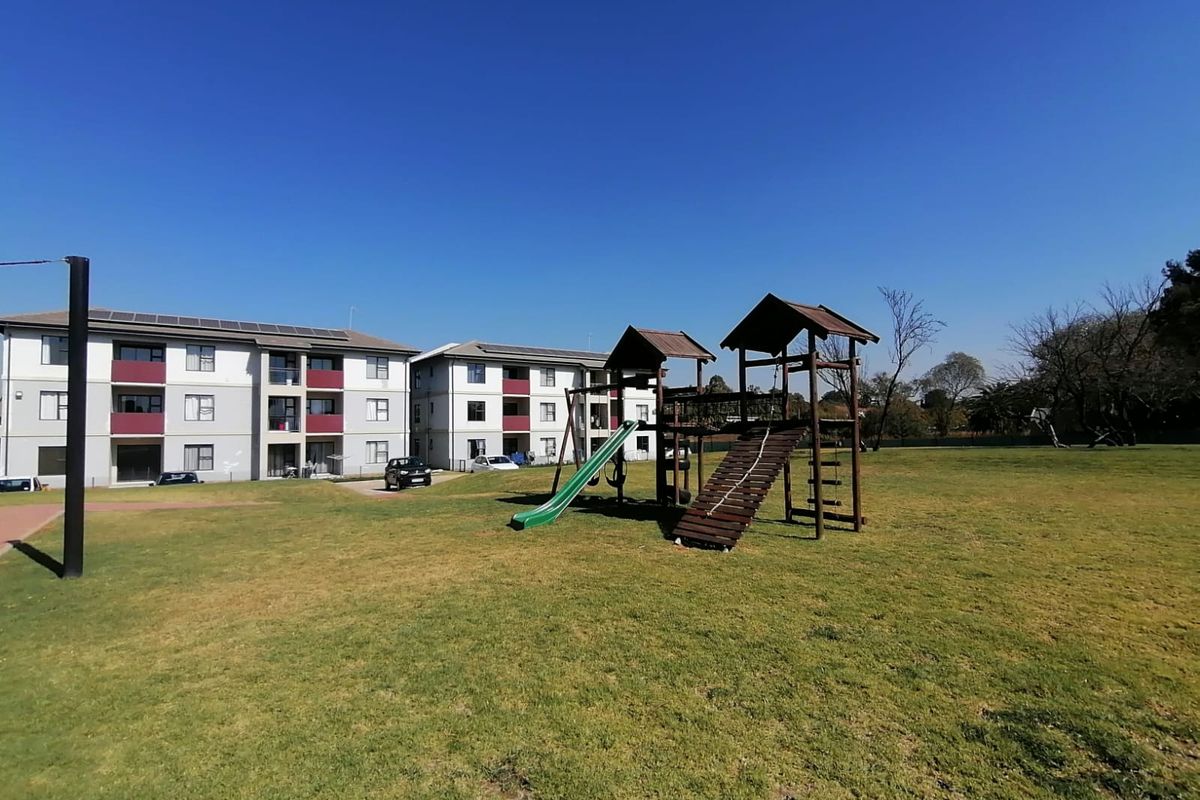 Spacious communal garden area featuring a children's playground set and well-maintained lawn, situated within a townhouse complex.