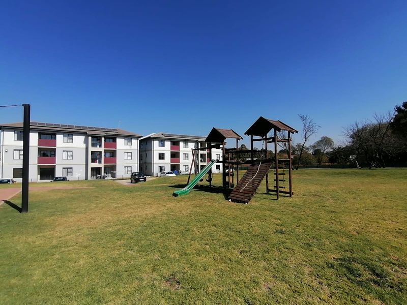 Spacious communal garden area featuring a children's playground set and well-maintained lawn, situated within a townhouse complex.