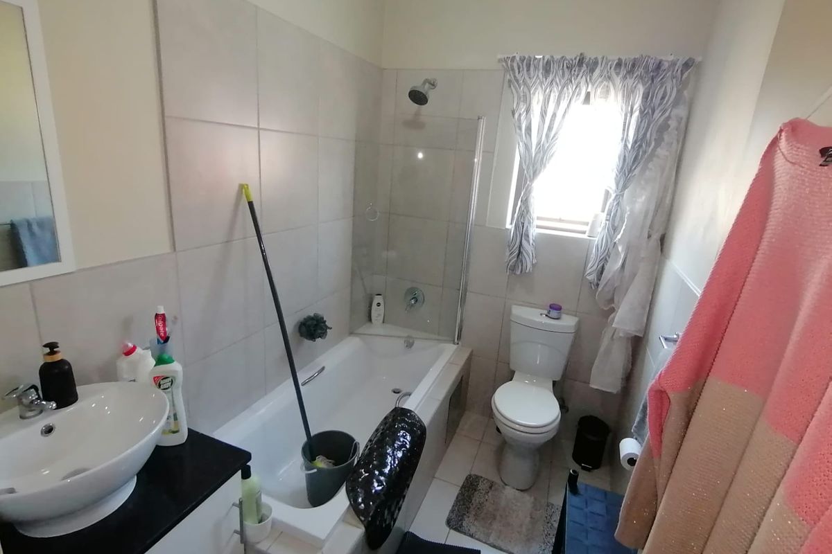 A functional bathroom featuring a built-in vanity with a vessel sink, a bathtub with a glass shower screen, and a standard toilet.