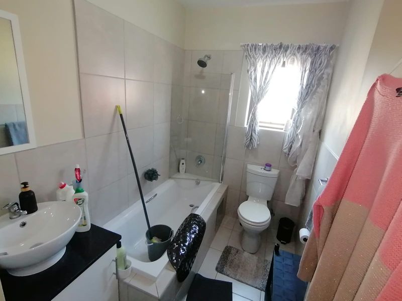 A functional bathroom featuring a built-in vanity with a vessel sink, a bathtub with a glass shower screen, and a standard toilet.