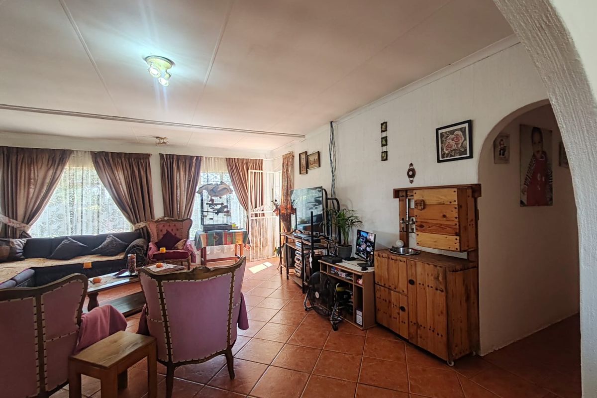 A spacious living room featuring terracotta floor tiles, an arched entryway, and large windows allowing for natural light.