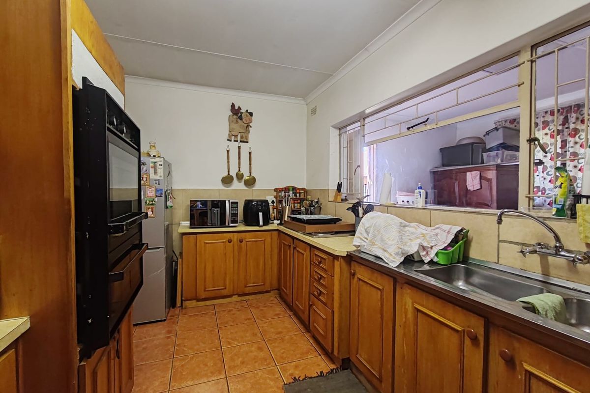 A functional kitchen featuring wooden cabinetry, a built-in eye-level oven, stainless steel sink, and tiled flooring with a window overlooking an adjacent space.