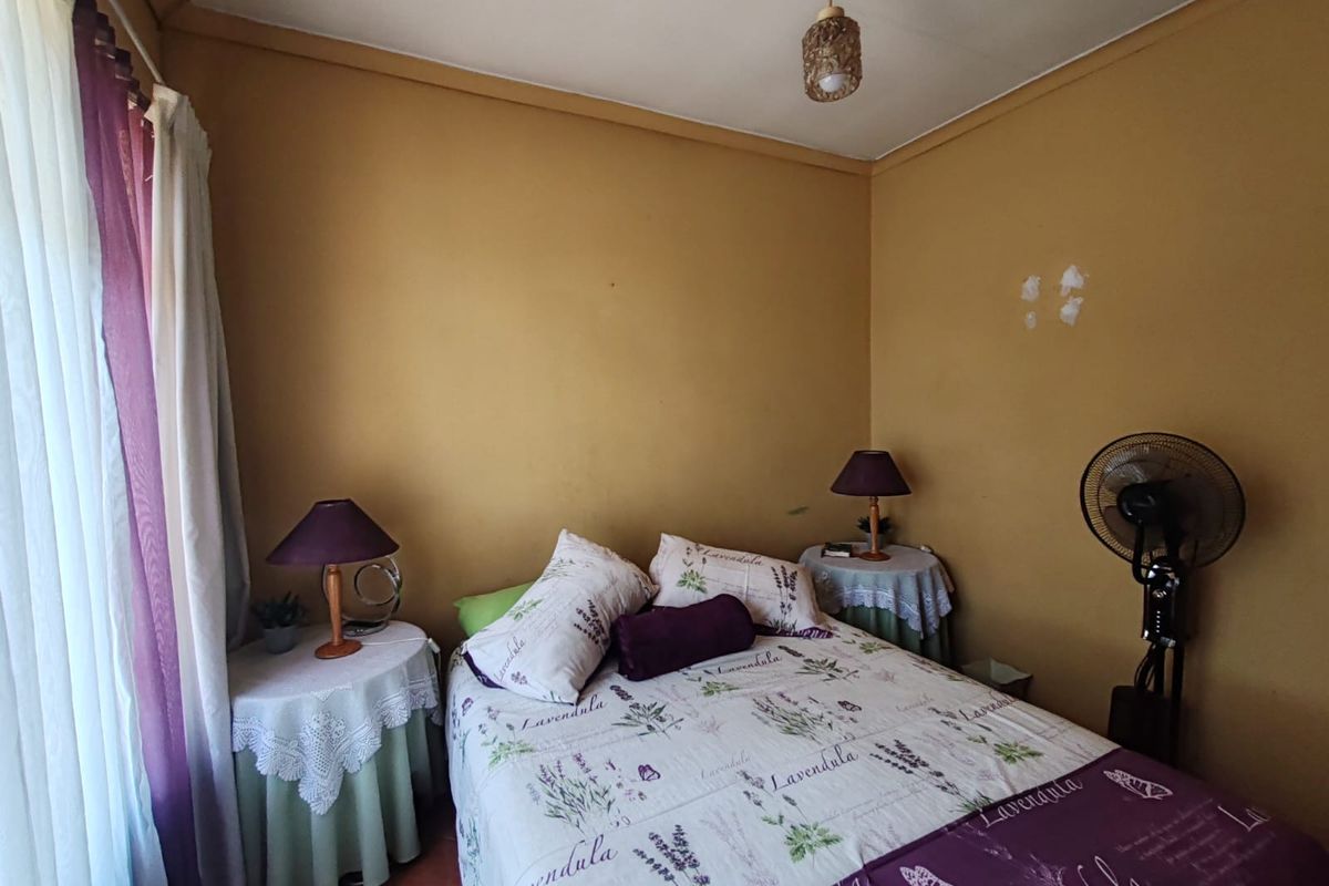 A bedroom featuring terracotta floor tiles and mustard-colored walls, providing a functional space with potential for cosmetic updates.