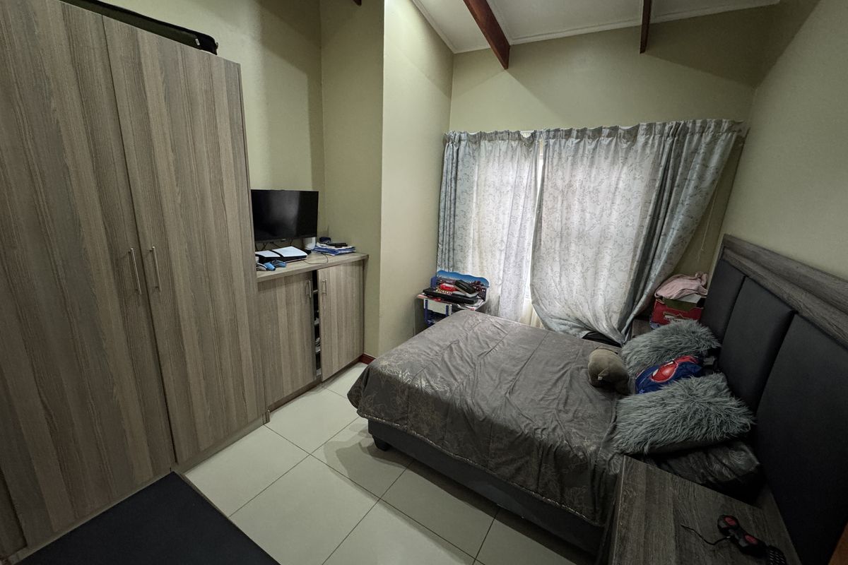 A bedroom featuring high vaulted ceilings with exposed timber beams, tiled flooring, and built-in wooden cabinetry.