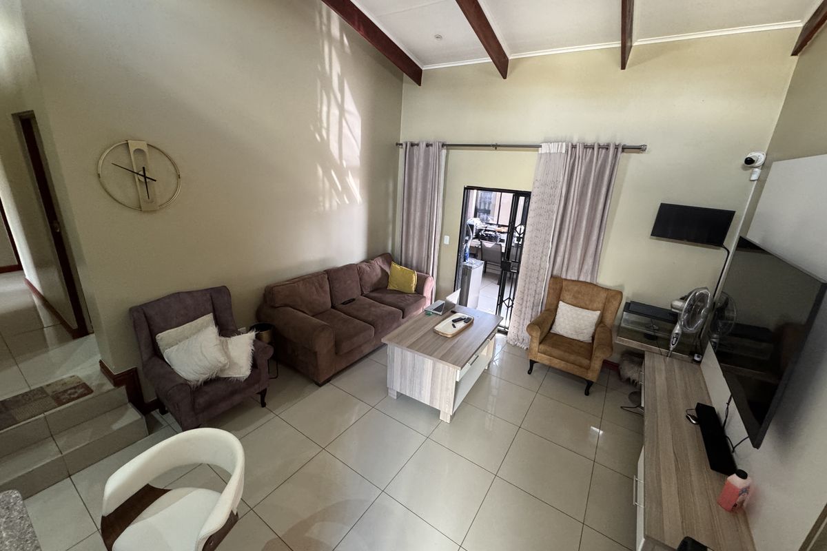 Spacious living room featuring high vaulted ceilings with exposed timber beams and large format floor tiles, providing an open and airy atmosphere.