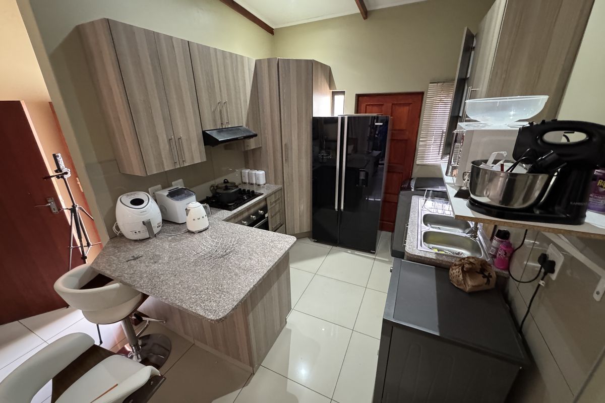 A functional kitchen featuring wood-look cabinetry, granite-style countertops, a built-in hob, extractor fan, and tiled flooring.