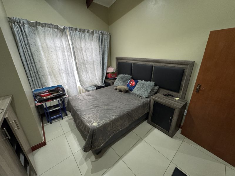 A bedroom featuring tiled flooring, a vaulted ceiling, and a built-in headboard with integrated bedside cabinetry.