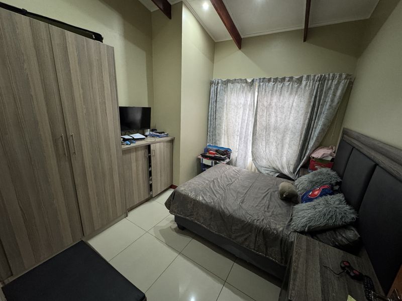 A bedroom featuring high vaulted ceilings with exposed timber beams, tiled flooring, and built-in wooden cabinetry.
