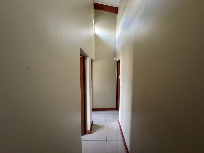 A bright hallway featuring high vaulted ceilings with exposed timber beams and neutral tiled flooring, providing access to multiple rooms.
