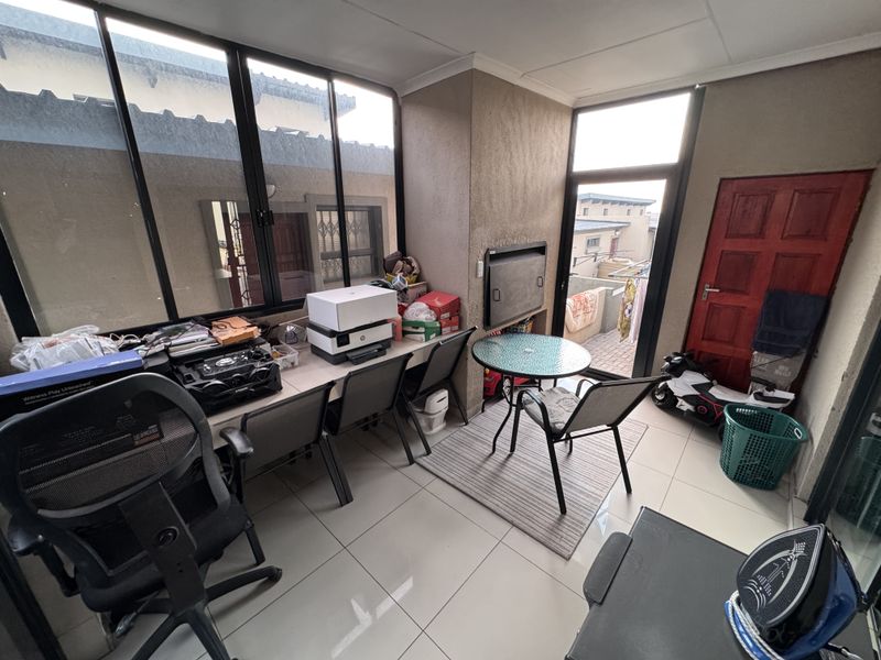 A sunroom or enclosed patio area featuring large windows, tiled flooring, and a built-in fireplace, offering a versatile space for relaxation or work.