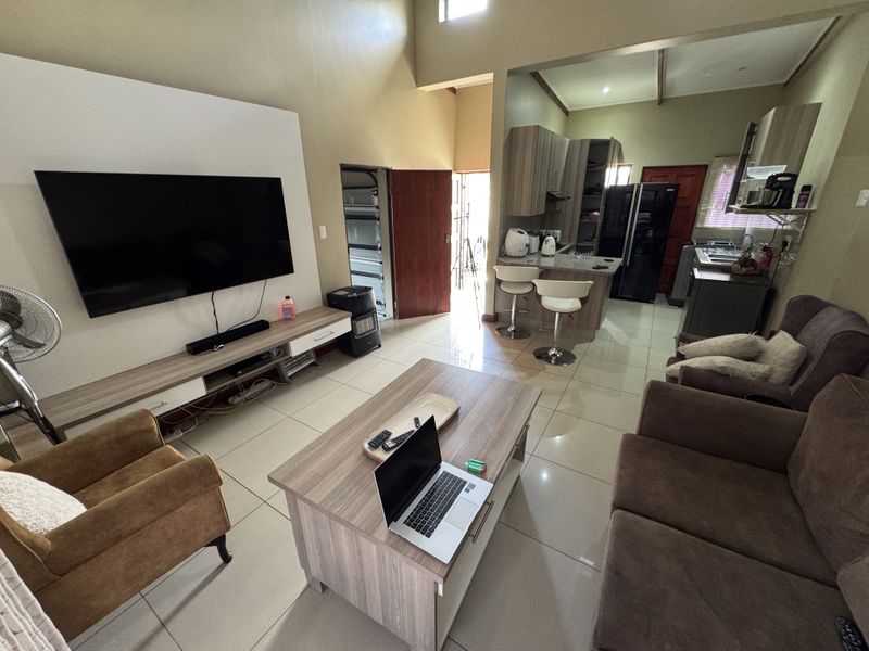 Open-plan living area featuring tiled flooring, high ceilings, and a modern kitchen with breakfast bar, seamlessly flowing into the main lounge space.