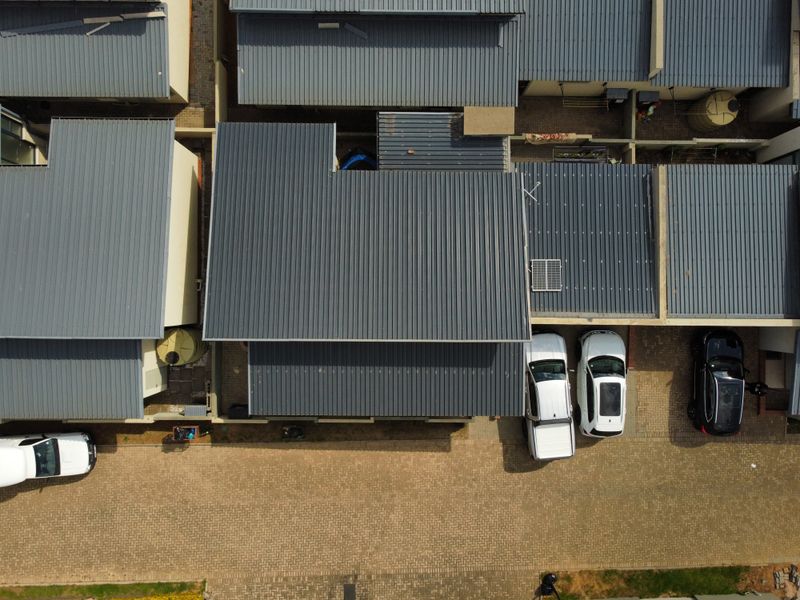 Aerial view of a residential property complex featuring corrugated metal roofing, paved driveway areas, and integrated solar panels.