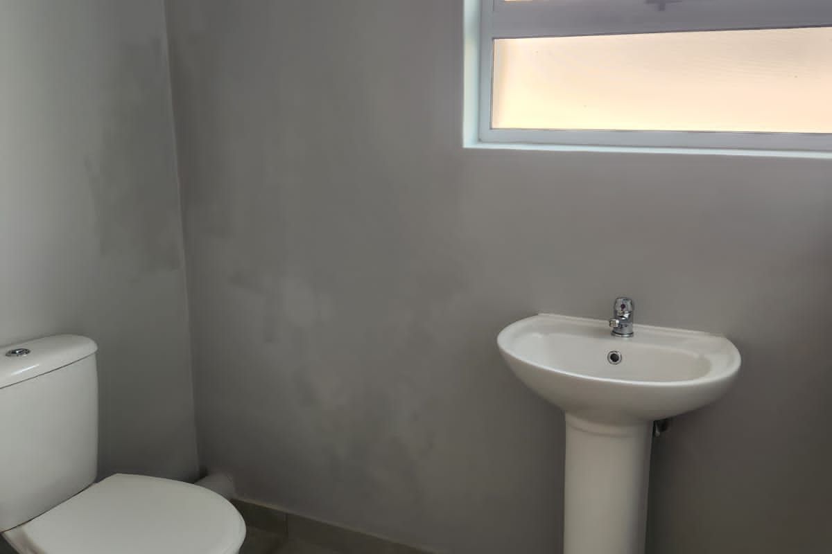 A functional bathroom featuring a pedestal basin, a standard toilet, and tiled flooring with a window for natural light.