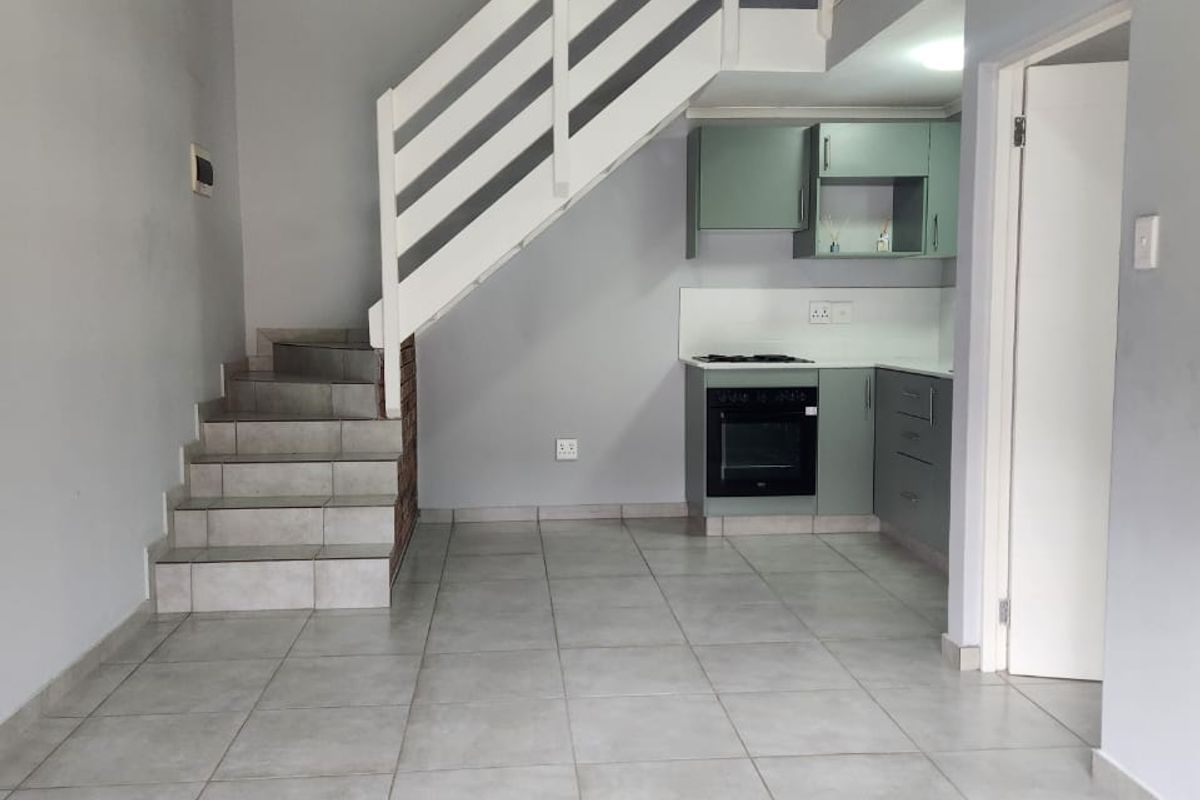 Open plan living area featuring tiled flooring, a compact kitchen with built-in cabinetry, and a staircase leading to an upper level.