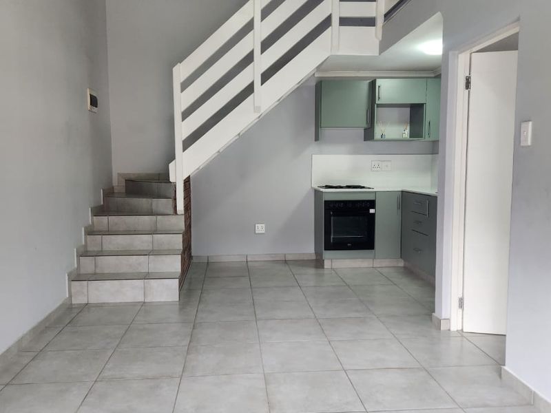 Open plan living area featuring tiled flooring, a compact kitchen with built-in cabinetry, and a staircase leading to an upper level.