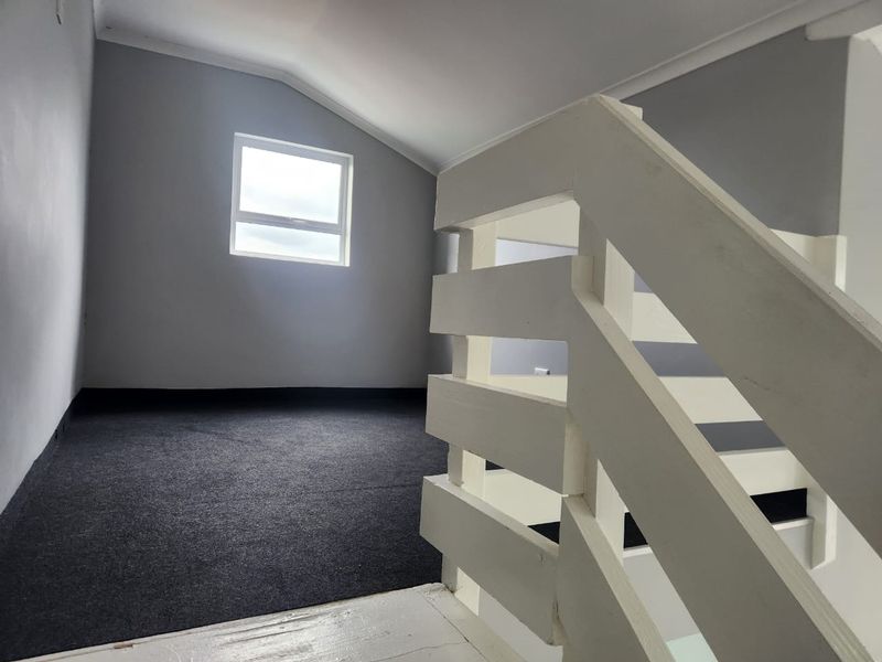 An upper-level landing area featuring dark carpeting, a white timber staircase railing, and a single window providing natural light.