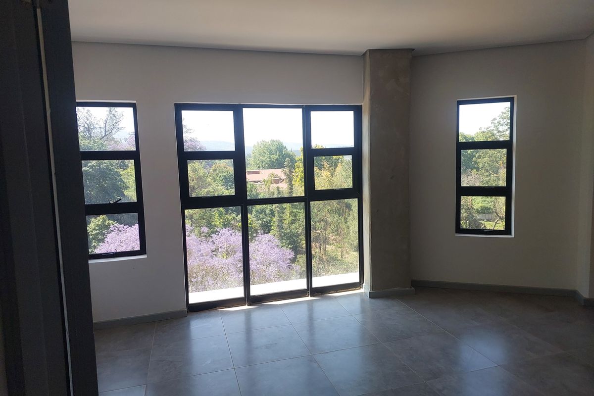 A bright, empty bedroom featuring large black-framed windows that offer scenic views of the surrounding trees and greenery.