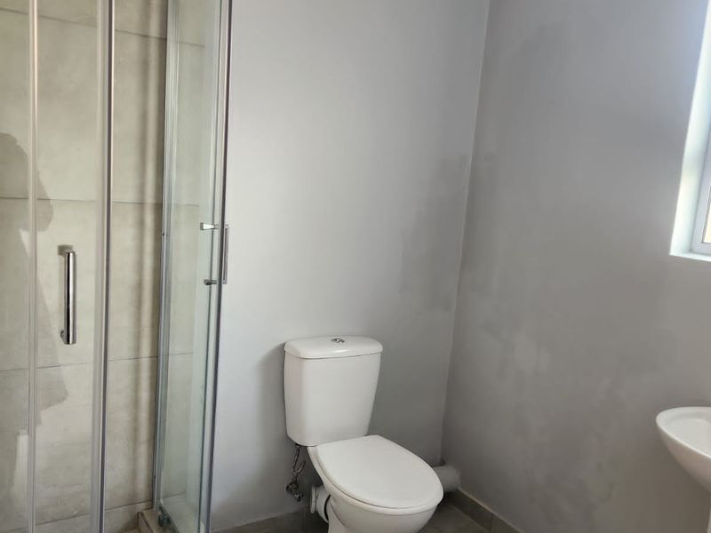 A functional bathroom featuring a glass-enclosed shower, a standard white toilet, and a pedestal sink with neutral floor tiling.