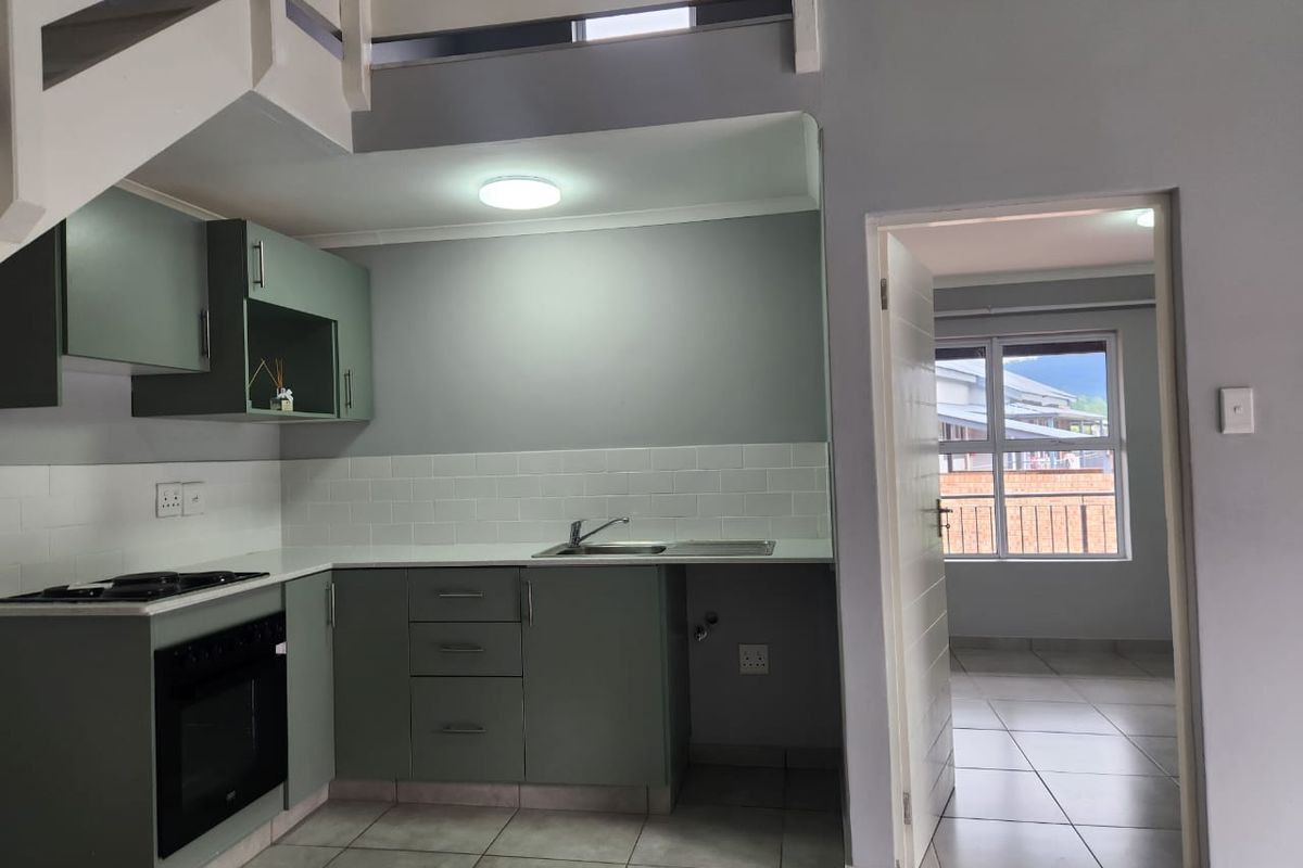 Modern kitchen featuring sage green cabinetry, white subway tile backsplash, built-in oven and hob, with an adjacent room visible through the doorway.