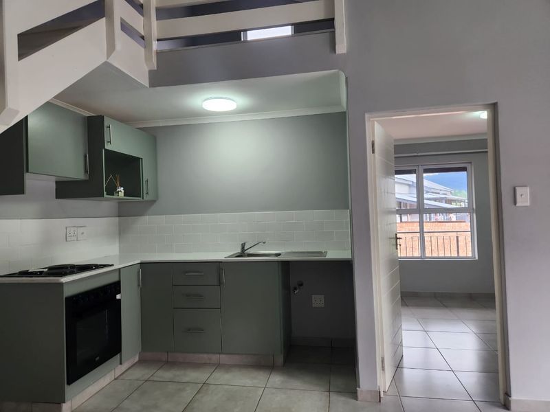 Modern kitchen featuring sage green cabinetry, white subway tile backsplash, built-in oven and hob, with an adjacent room visible through the doorway.