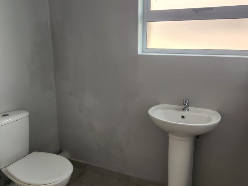 A functional bathroom featuring a pedestal basin, a standard toilet, and tiled flooring with a window for natural light.
