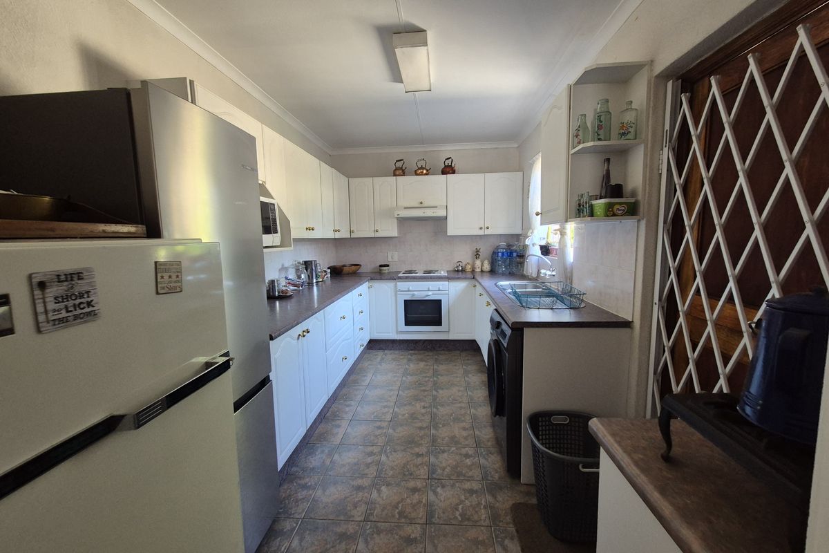 A functional galley-style kitchen featuring white cabinetry, built-in oven, hob, extractor fan, and tiled flooring with integrated laundry appliance space.