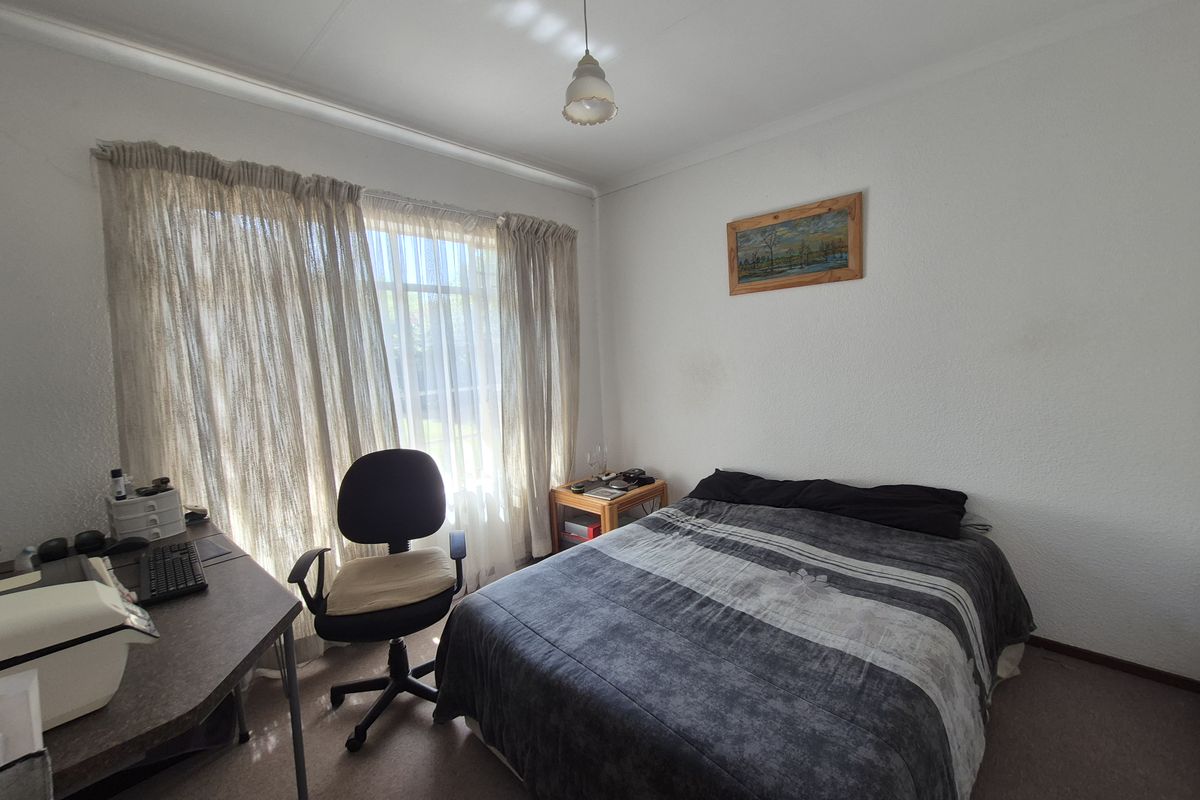 A functional bedroom featuring carpeted flooring, a large window with curtains, and a central light fixture.