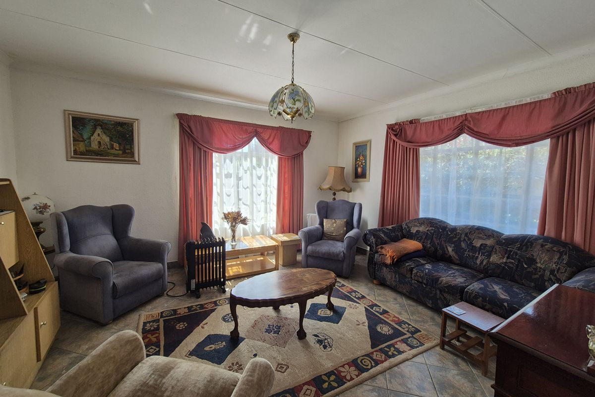A traditional living room featuring tiled flooring, large windows with draped curtains, and a central pendant light fixture.