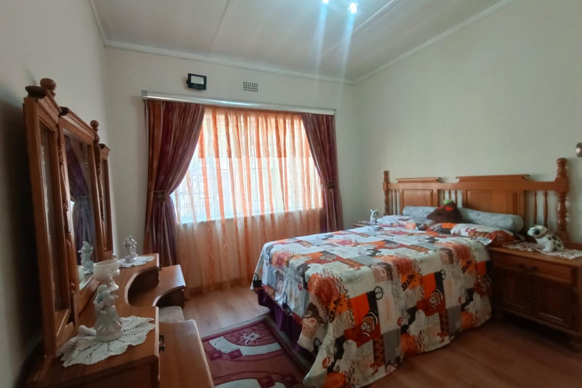 A bedroom featuring laminate flooring, a large window with curtains, and a ceiling-mounted light fixture.