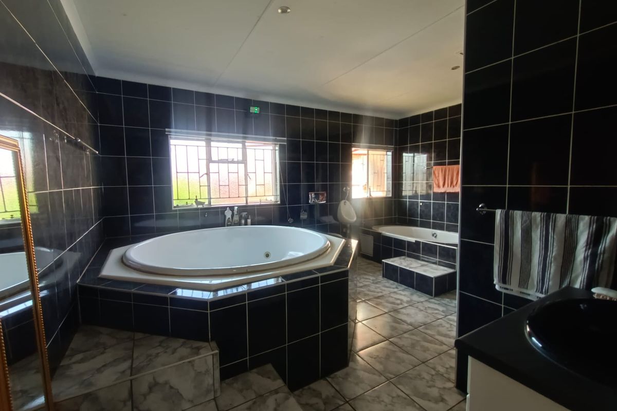 Spacious bathroom featuring a large corner jetted tub, a secondary built-in bathtub, and dark wall tiling throughout.