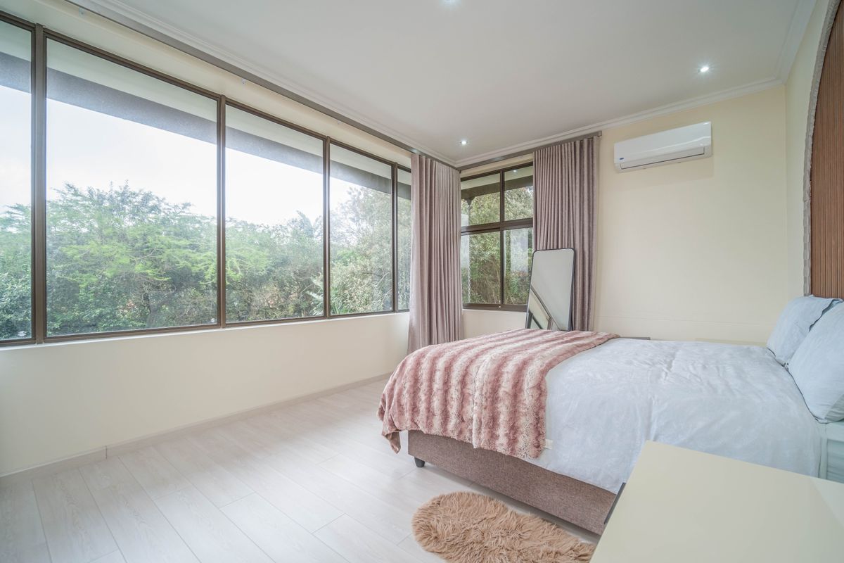 A bright and spacious bedroom featuring large floor-to-ceiling windows, light wood-look flooring, and a wall-mounted air conditioning unit.