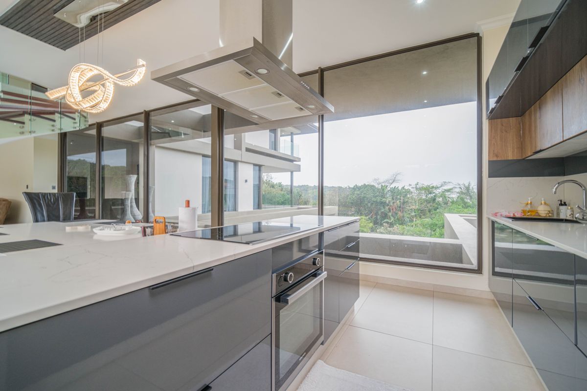 Modern kitchen featuring sleek cabinetry, stone countertops, integrated oven and cooktop, and large floor-to-ceiling windows offering expansive views.