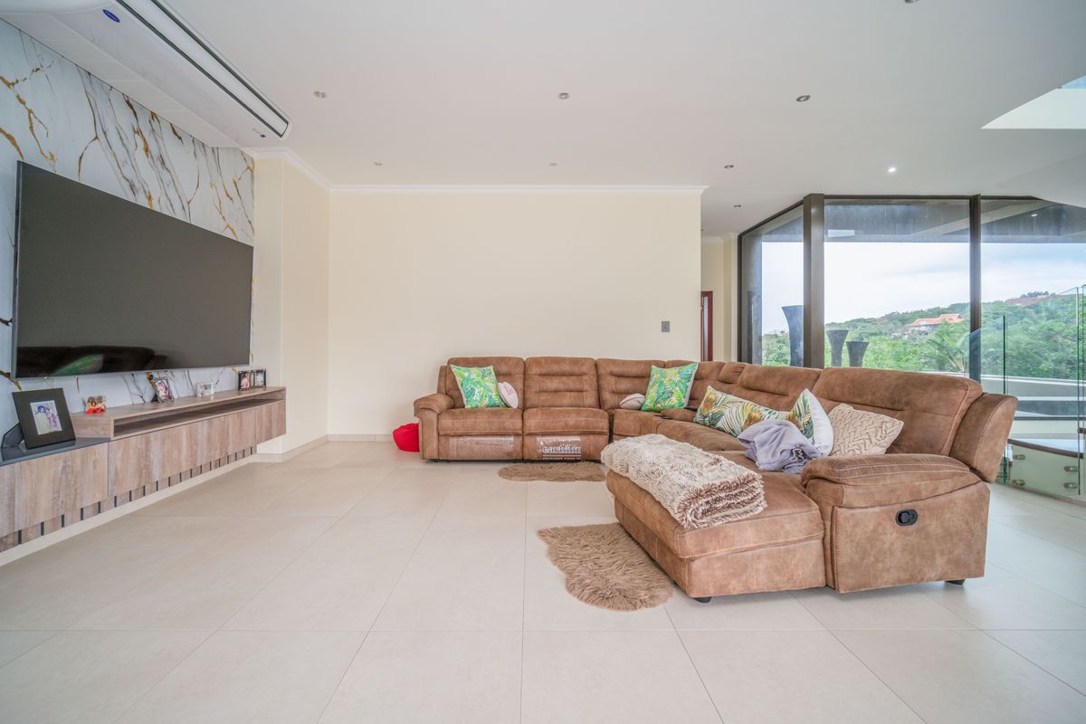 Spacious living room featuring large format floor tiles, a marble-effect feature wall, wall-mounted cabinetry, and floor-to-ceiling glass doors leading to an outdoor area.