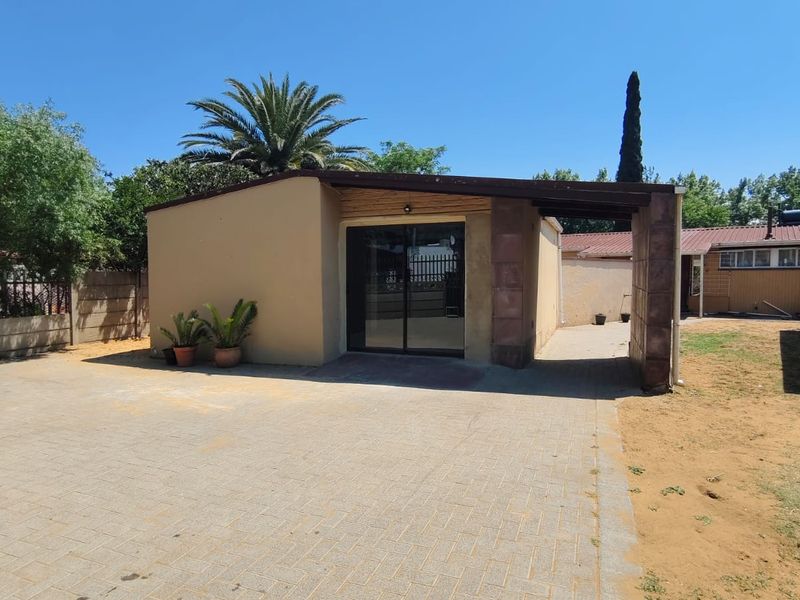 Rear exterior view featuring a paved driveway, a covered patio area with stone-clad pillars, and sliding glass doors leading into the property.