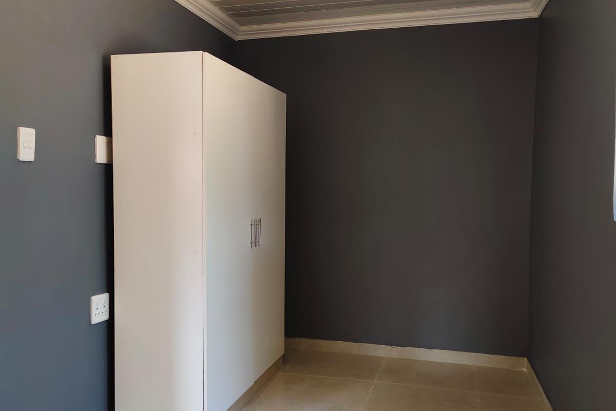 A clean bedroom featuring dark grey walls, tiled flooring, a built-in wardrobe, and a white tongue and groove ceiling with crown moulding.