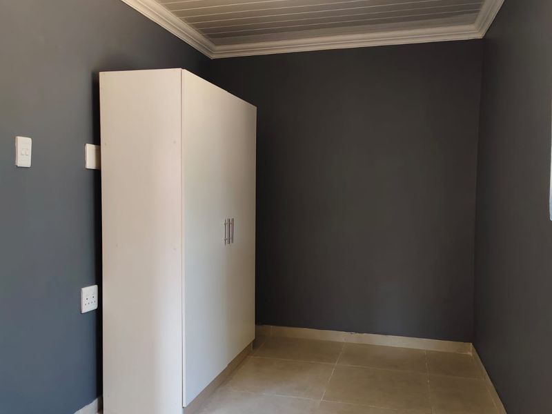 A clean bedroom featuring dark grey walls, tiled flooring, a built-in wardrobe, and a white tongue and groove ceiling with crown moulding.
