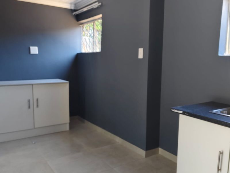 A clean, functional scullery area featuring built-in cabinetry, a sink, tiled flooring, and a modern tongue and groove ceiling finish.
