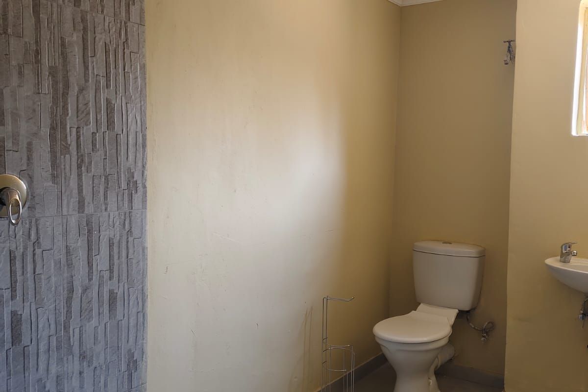 A functional bathroom featuring a walk-in shower with stone-look cladding, a standard toilet, and a wall-mounted basin with tiled flooring.