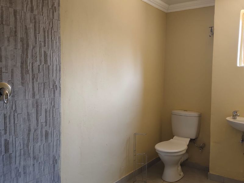 A functional bathroom featuring a walk-in shower with stone-look cladding, a standard toilet, and a wall-mounted basin with tiled flooring.