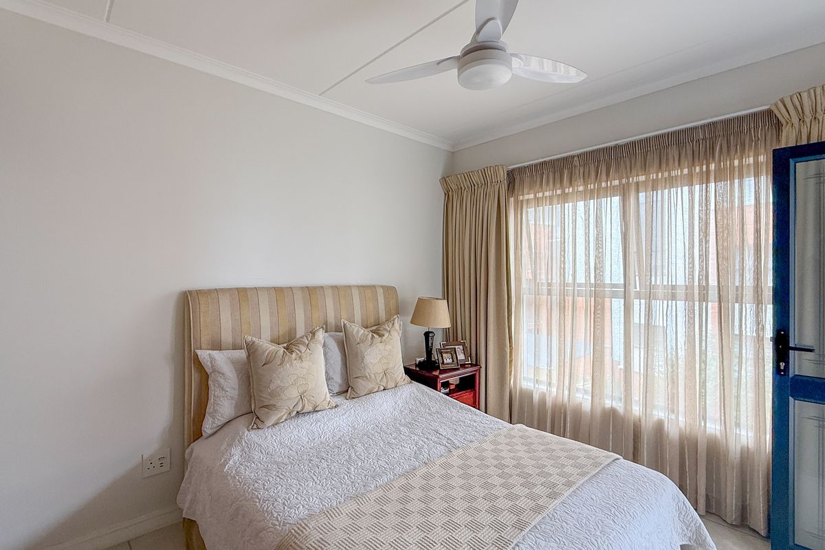 A well-maintained bedroom featuring built-in cupboards, a ceiling fan, and large windows with curtain tracks, offering a bright and comfortable living space.