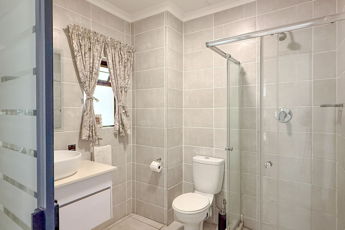 A modern bathroom featuring floor-to-ceiling neutral tiling, a glass-enclosed shower, a vanity with a vessel sink, and a toilet.