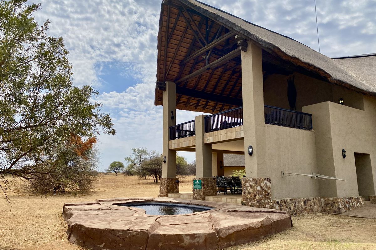 A two-story thatched-roof residence featuring a covered patio, balcony, and a natural stone-surround plunge pool set in a dry landscape.